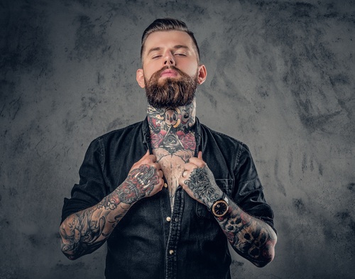 Studio portrait of bearded hipster man with tattoos on his arms, chest and neck